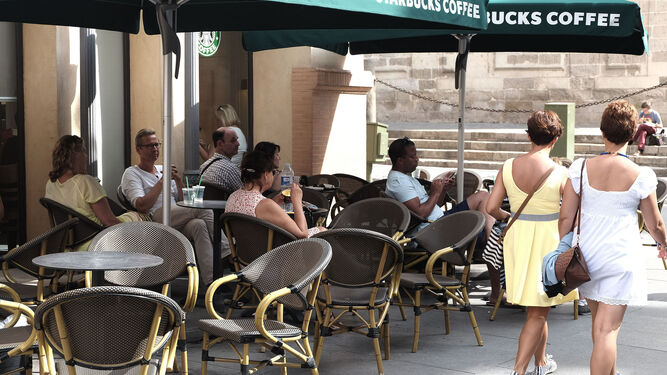 Una pareja de turistas pasa junto a los veladores del Starbucks de la Avenida.