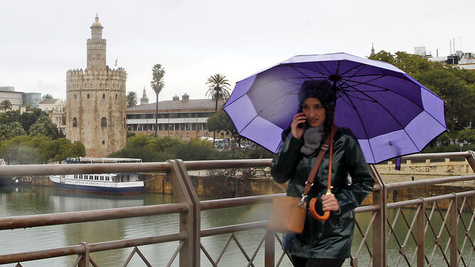 Una joven camina bajo la lluvia por el puente de San Telmo.