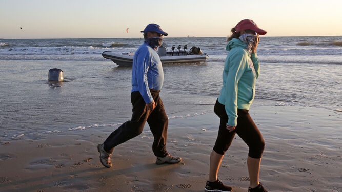 Dos vecinos de Las Redes, en El Puerto, pasean con sus mascarillas delante de una narcolancha