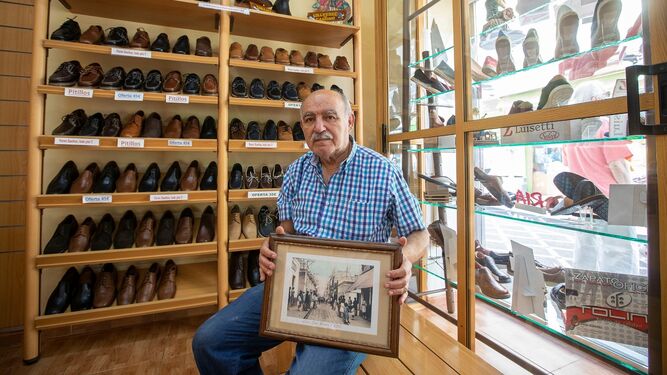 El veterano comerciante Juan Luis Ruiz posa en la zapatería San Rafael (La Infantil) con una fotografía histórica de la calle San Rafael, donde se asienta el comercio.