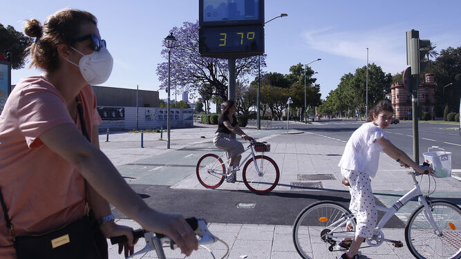 Jóvenes pasean en bicicleta en Sevilla, con un termómetro marcando 37º.