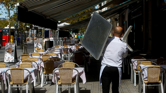 Un camarero retira una mesa de un restaurante barcelonés ante la entrada en vigor este viernes del cierre de bares y restaurantes.