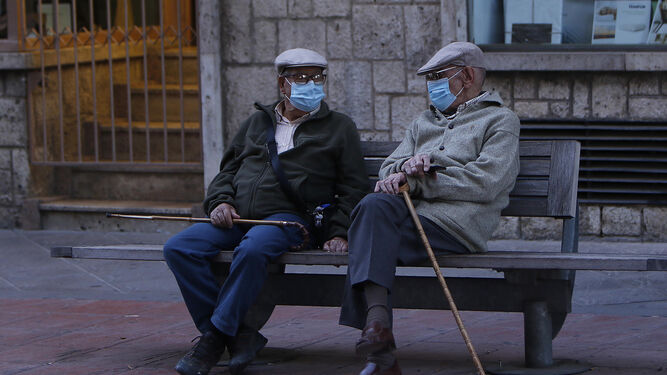 Dos ancianos conversan en un banco con mascarilla.